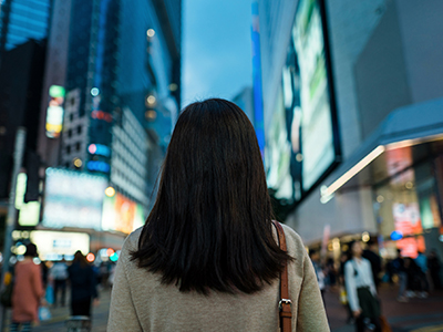 A woman walks down a busy city street. / Une femme marchant dans une rue achalandée.