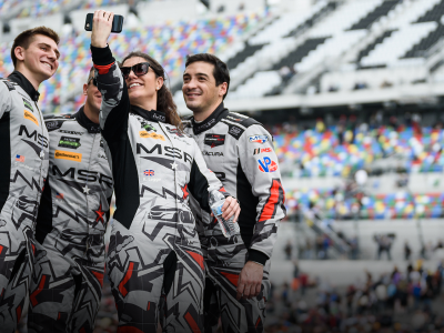 Group shot of an Acura pit crew taking a selfie on the track with stadium seating visible in the background.	Photo d’une équipe de ravitaillement Acura prenant un égoportrait sur un circuit de course avec des estrades en arrière-plan.